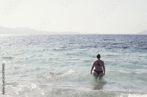 Silhouette of attractive plus size woman going into the water for a sunset swim. Curvy girl at vacation in Mallorca, Balearics, Spain. Social distancing during coronavirus. Self-acceptance.