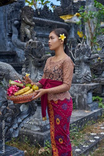 Asian girl. Beautiful Balinese women in traditional dress with yellow plumeria frangipani flower makes offering for Gods near the temple. Balinese tradition.