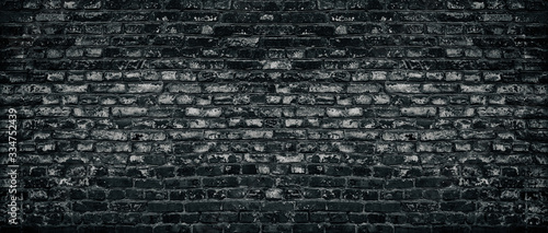Old black shabby brick wall wide texture. Aged dark brickwork with peeling paint. Gloomy grungy widescreen background
