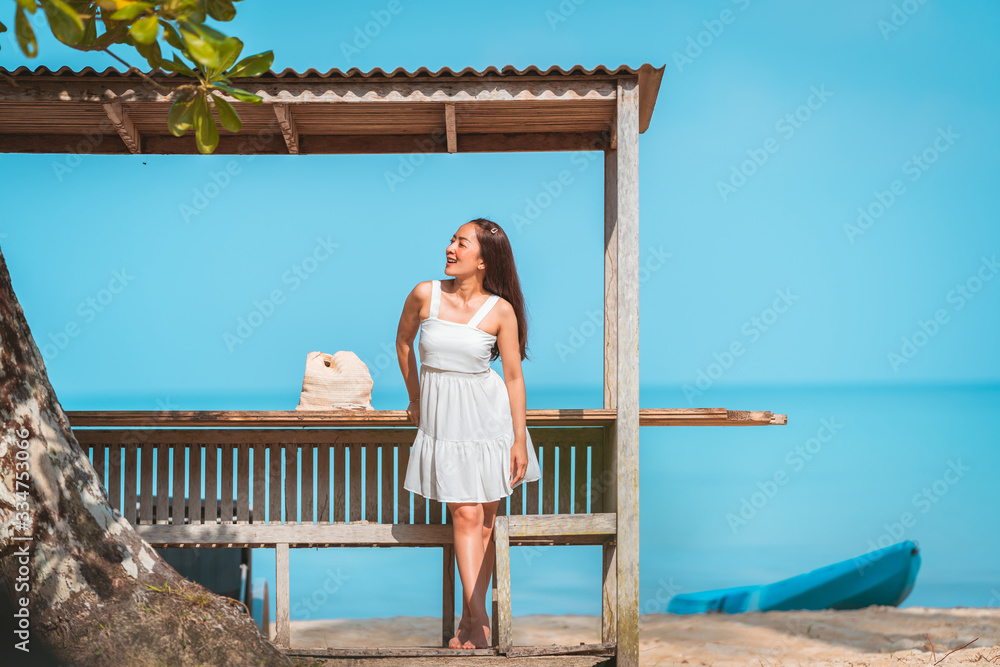 asian girl in white dress by posing relax in bench wood on the beach with sunlight shine