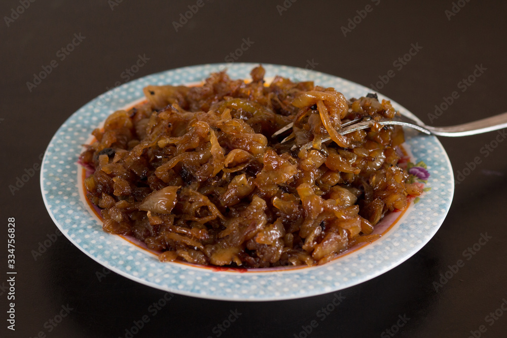 Close up caramelized onion on plate with fork on the black background Close up caramelized onion on plate with fork on the black background