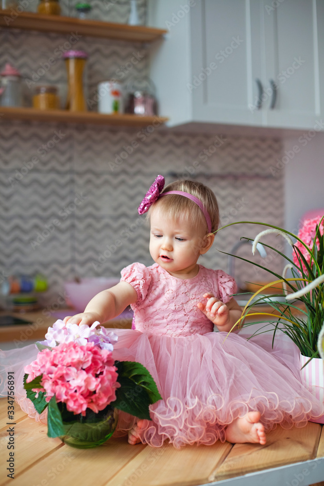 a child in a festive pink dress in the kitchen with flowers a child in a festive pink dress in the kitchen with flowers