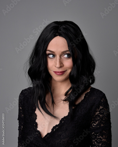 Close up portrait of a pretty, goth girl with dark hair posing in front a studio background.