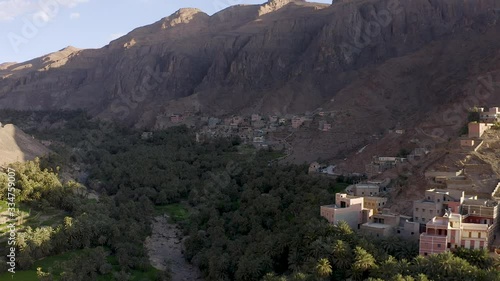 A sunrise or sunset aerial straif or passing shot of a village nestled in a lush valley of palms encircled by a steep headwall of jagged, desert, mountain peaks. photo