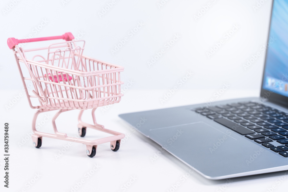 Online shopping. Mini empty pink shop cart trolley over a laptop computer on white table background, buying at home concept, close up