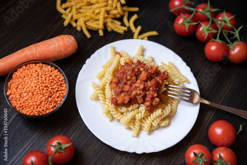 Makaroni mit veganer Nudelsoße a la Bolognese aus roten Linsen, Tomaten und Möhren auf schwarzen Untergrund aus Holz photo