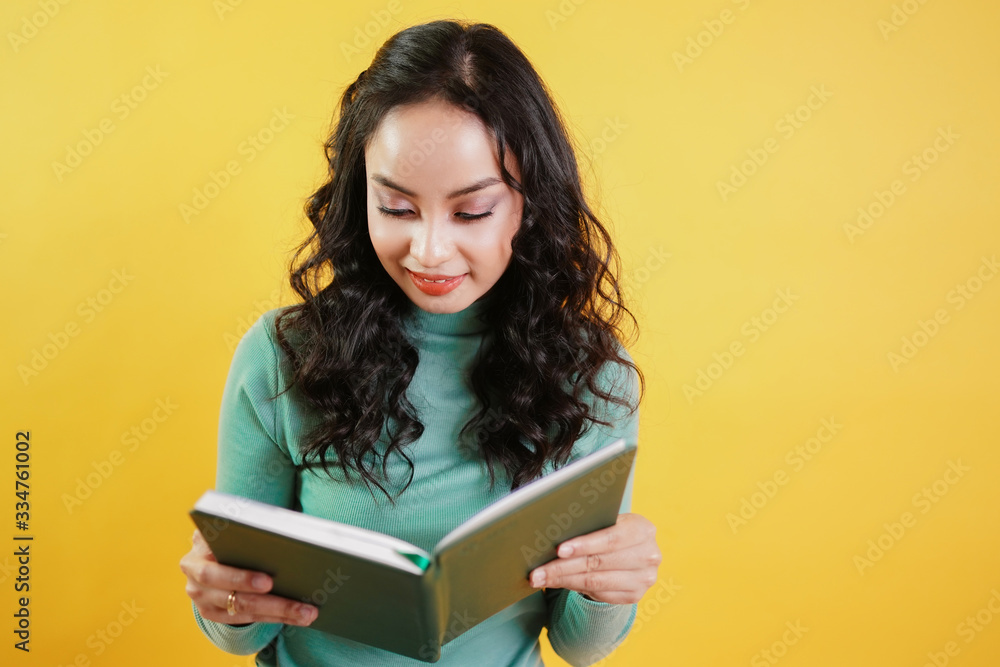 young attractive asian woman reads a book isolated on Yellow background. Intelligent girl reading the book for knowledge. young attractive asian woman reads a book isolated on Yellow background. Intelligent girl reading the book for knowledge.