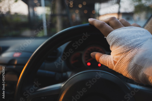 Closeup of injured hand with white bandage holding steering wheel with blurred cafe background, Unsafe driving concept