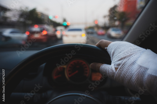 Closeup of injured hand with white bandage holding steering wheel with blurred cars background, Unsafe driving concept