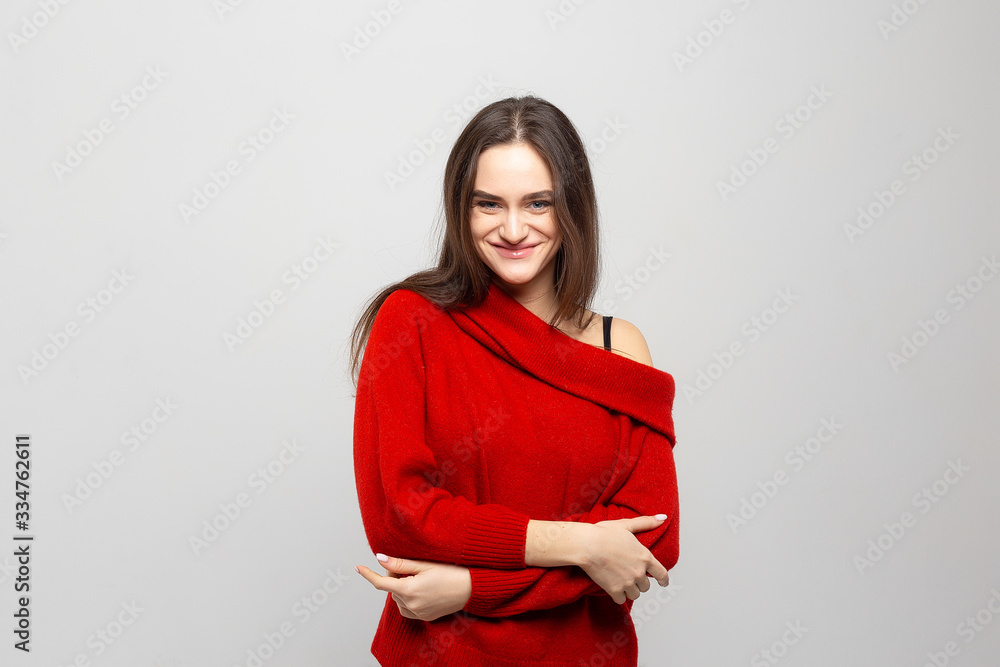 Portrait of a young beautiful woman with a light smile dressed in a red sweater on a light gray background. Portrait of a young beautiful woman with a light smile dressed in a red sweater on a light gray background.
