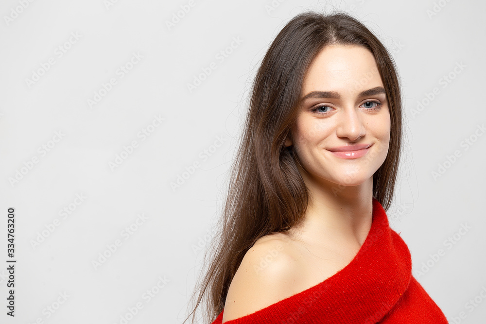 Portrait of a young beautiful woman with a light smile dressed in a red sweater on a light gray background. Portrait of a young beautiful woman with a light smile dressed in a red sweater on a light gray background.