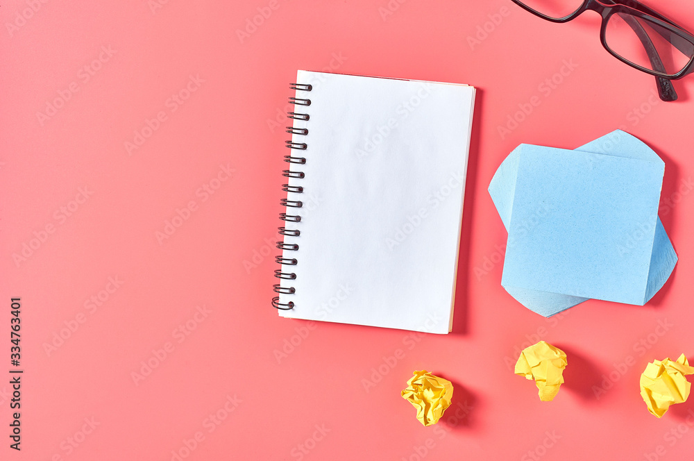 Blank notepad near crumpled paper balls and modern glasses on pink desk. Education or business concept Blank notepad near crumpled paper balls and modern glasses on pink desk. Education or business concept