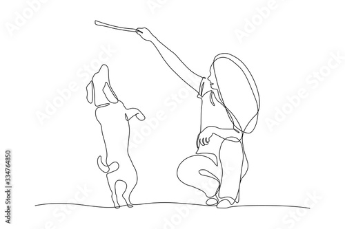 Woman training dog with stick in continuous line art drawing style. Owner playing with her cute dog on a walk. Black linear sketch isolated on white background. Vector illustration