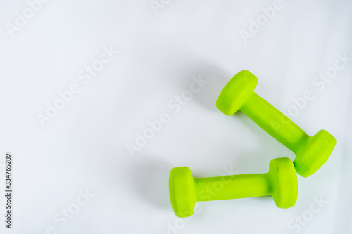Two green dumbbells on a white background. Stay at home and exercise. Coronavirus. Space for text