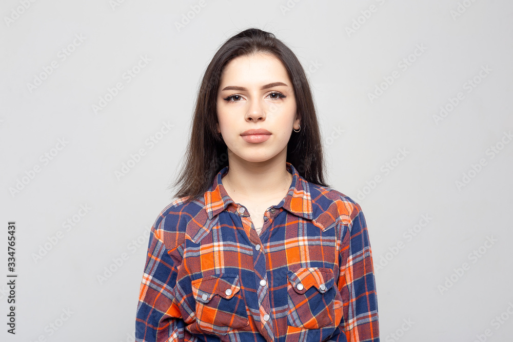 Portrait young beautiful woman not smiling in plaid shirt isolated on white-gray background. Girl with minimal natural make-up on her face. The photo is not retouched with natural defects on the skin. Portrait young beautiful woman not smiling in plaid shirt isolated on white-gray background. Girl with minimal natural make-up on her face. The photo is not retouched with natural defects on the skin.