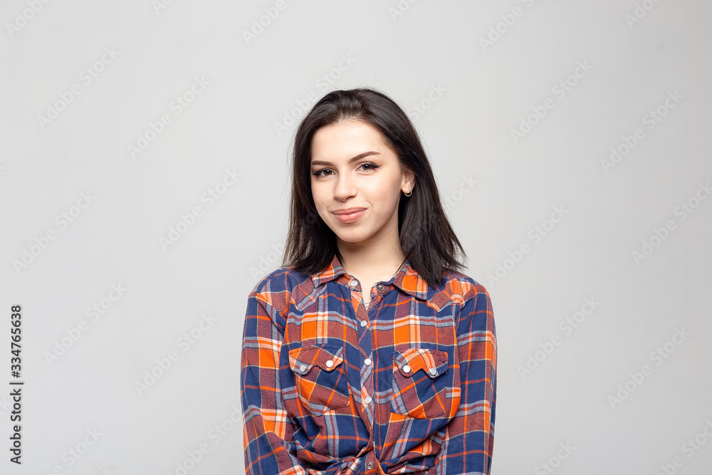 Portrait young beautiful woman not smiling in plaid shirt isolated on white-gray background. Girl with minimal natural make-up on her face. The photo is not retouched with natural defects on the skin. Portrait young beautiful woman not smiling in plaid shirt isolated on white-gray background. Girl with minimal natural make-up on her face. The photo is not retouched with natural defects on the skin.