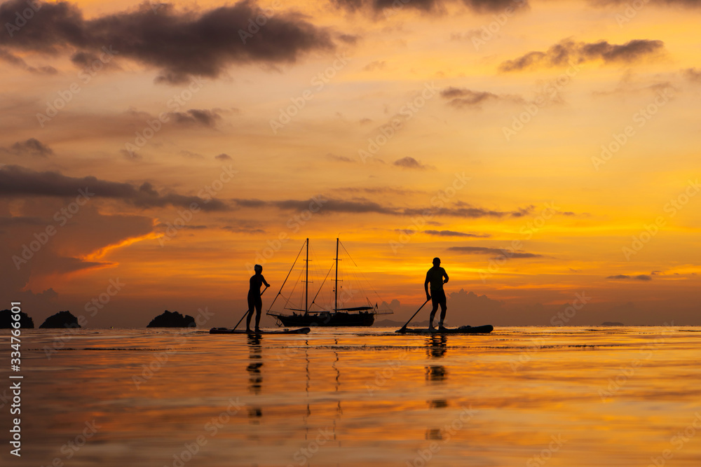 Colorful sunset on a tropical beach. Orange sunset on the ocean. Colorful sunset in the tropics. A pair of people are swimming on sup boards