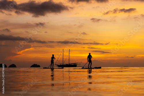 Wallpaper Mural Colorful sunset on a tropical beach. Orange sunset on the ocean. Colorful sunset in the tropics. A pair of people are swimming on sup boards Torontodigital.ca
