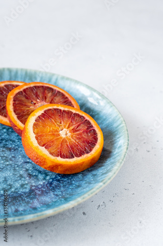 Red blood orange lies on a blue-green plate on a white concrete background