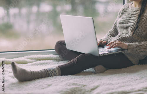 Young woman with laptop sitting home by the window, social media or home office concept
