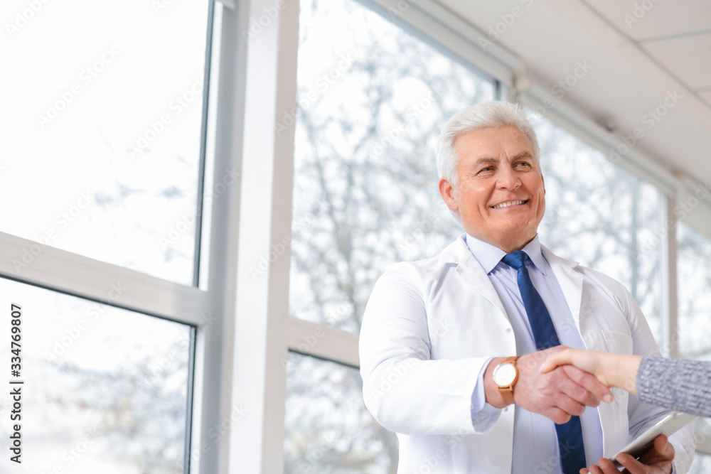Male doctor with patient shaking hands in clinic