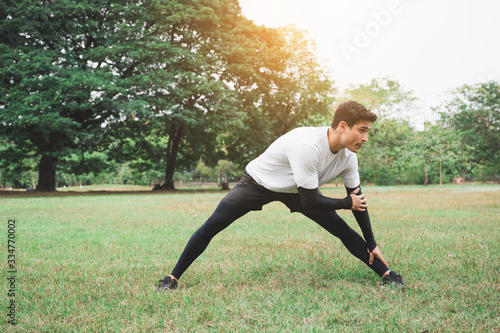 Young man runner stretching for warming up before running or working out in park.