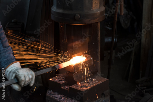 El herrero forjando manualmente el metal en máquina. Sonriente con fuegos y chispas.