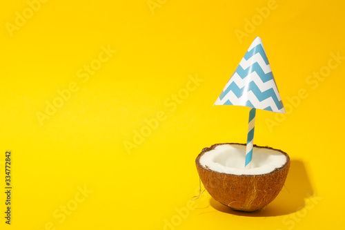 Coconut with beach umbrella on yellow background, space for text