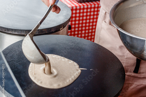 Making crepes pancakes in food market. A hand is making crepes outdoors pouring the batter onto a metal griddle.