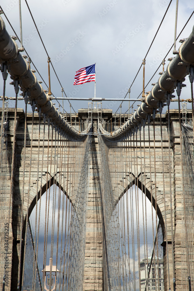 Fototapeta premium Architectural detail of the Brooklyn Bridge on which the American flag is flying