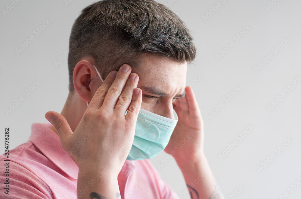 Portrait of ill dark hair european man in surgery face mask in pink polo having headache on white background Portrait of ill dark hair european man in surgery face mask in pink polo having headache on white background
