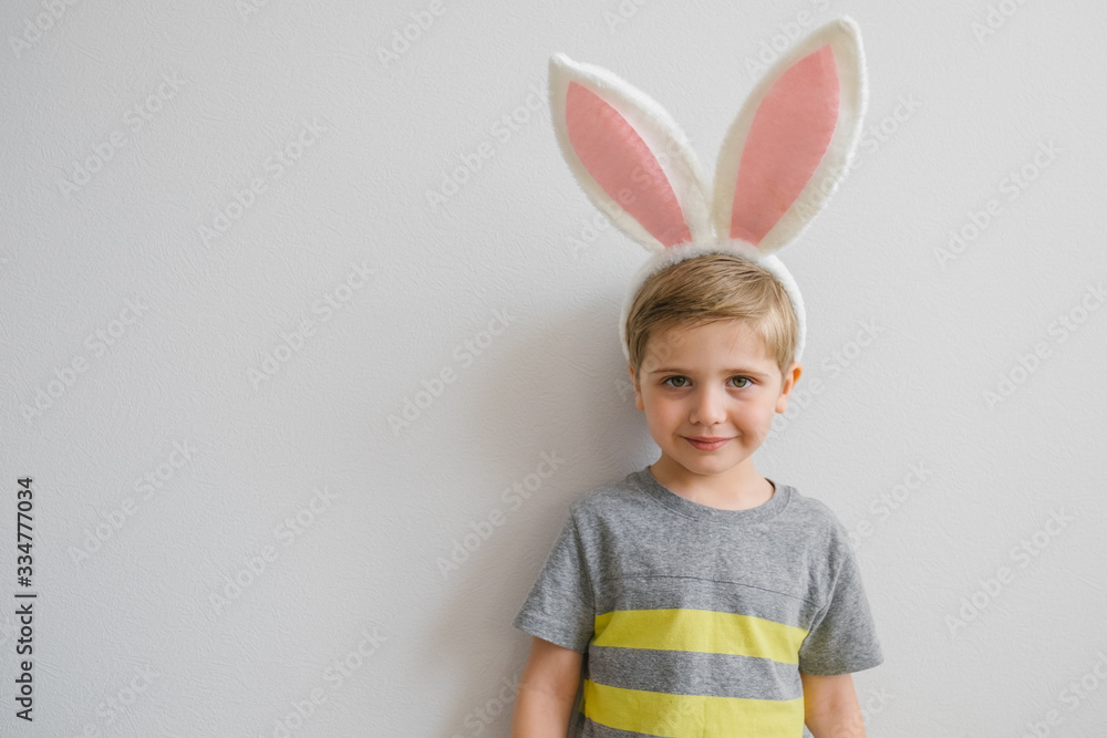 Boy in rabbit bunny ears on head on white studio background in striped grey and yellow t shirt. Cheerful crazy smiling happy child. Easter painting eggs on eyes. Easter and holidays. Happy easter! Boy in rabbit bunny ears on head on white studio background in striped grey and yellow t shirt. Cheerful crazy smiling happy child. Easter painting eggs on eyes. Easter and holidays. Happy easter!