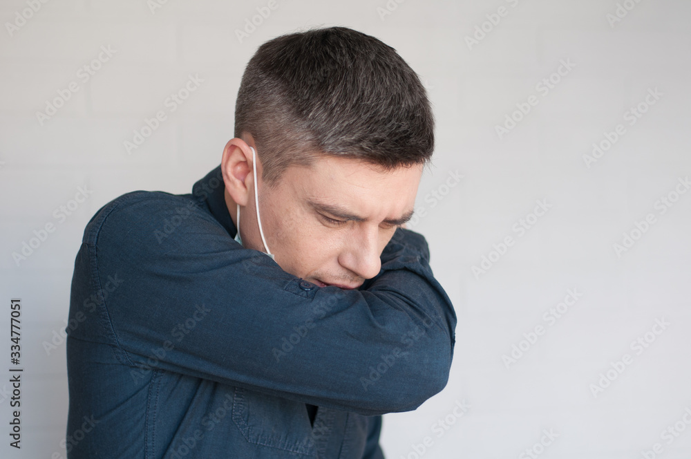 Portrait of coughing european dark hair man in surgery face mask in blue shirt on gray background Portrait of coughing european dark hair man in surgery face mask in blue shirt on gray background
