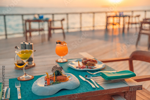 Fototapeta Naklejka Na Ścianę i Meble -  Luxury romantic sunset dinner table setup for couple in ocean view restaurant on tropical resort hotel outdoor restaurant with wine glasses and beautiful gourmet food

