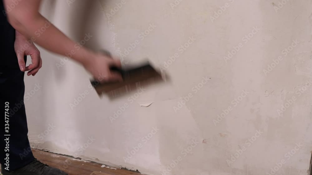 Muscular man with a wide spatula aligns the wall next to the floor. The painter applies putty, preparation for painting. Muscular man with a wide spatula aligns the wall next to the floor. The painter applies putty, preparation for painting.