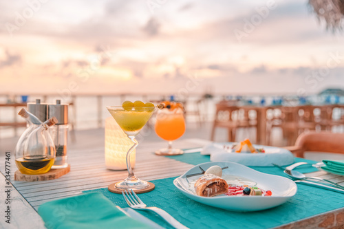 Fototapeta Naklejka Na Ścianę i Meble -  Luxury dinner food, cocktails on wooden table, with beautiful tropical resort, outdoor restaurant background, sunset time summer holiday and romantic vacation concept, luxury travel and lifestyle

