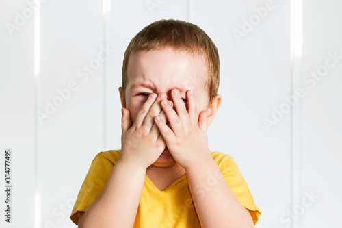 Crying baby boy in a yellow shirt covers his face with hands and shouts, tears