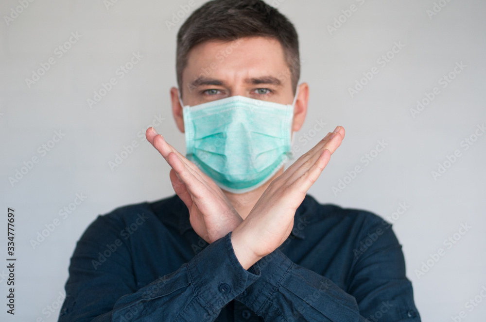 Portrait of european dark hair man in surgery face mask in blue shirt on gray background with crossed palms Portrait of european dark hair man in surgery face mask in blue shirt on gray background with crossed palms