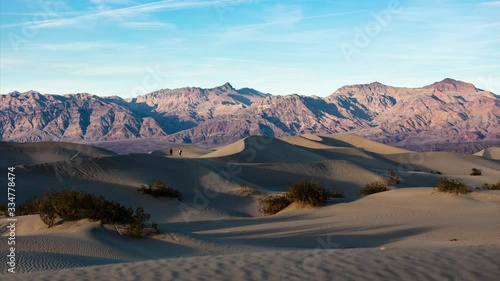 A time lapse of sunset at the Mesquite Flat Dunes in Death Valley National Park . Visitors walk across the dunes. The Funeral Mountains, part of the Amargosa Range, are seen in the background.