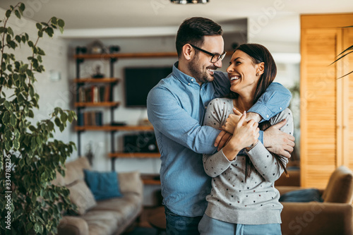 Real love. Couple hugging and smiling while standing in the living room, portrait. © bnenin