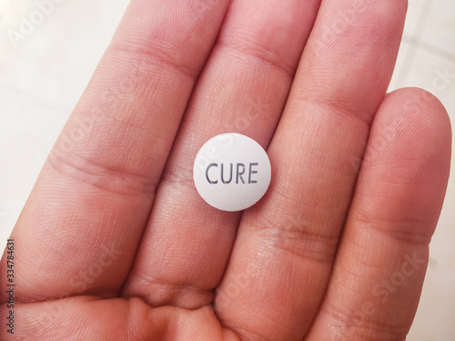 top view of a white pill with the text cure in hand - health concept - finding the cure