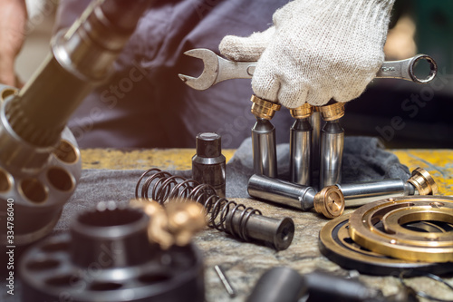 Professional mechanic man holding spanner tools for disassembly hydraulic piston pump, repair maintenance heavy machinery photo