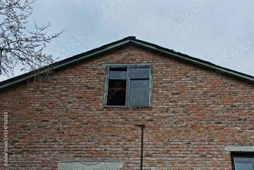 one brown old brick loft with one old window and broken glass against a gray sky © butus