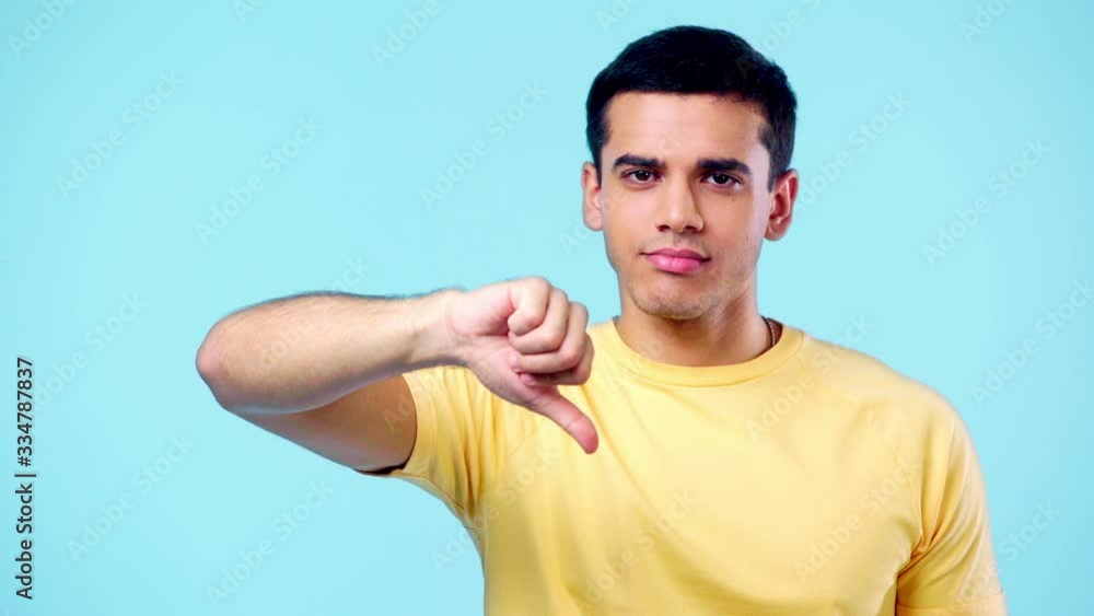 displeased man looking at camera and showing thumb down isolated on blue displeased man looking at camera and showing thumb down isolated on blue