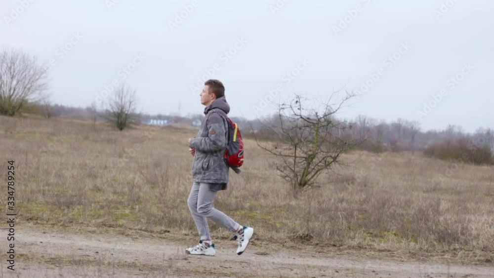 Man doing jogging on sandy road in flat area. Tourist male running with backpack through countryside in overcast cloudy weather. Man doing jogging on sandy road in flat area. Tourist male running with backpack through countryside in overcast cloudy weather.