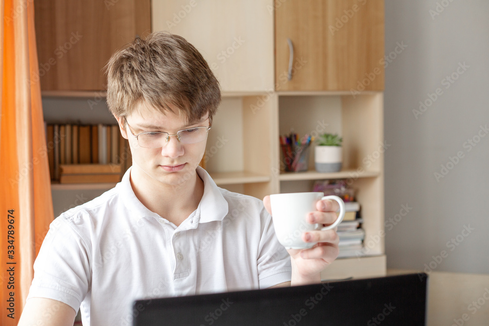 Student in glasses learning at home using laptop. Young man holding mug. Home school, online education, home education Student in glasses learning at home using laptop. Young man holding mug. Home school, online education, home education