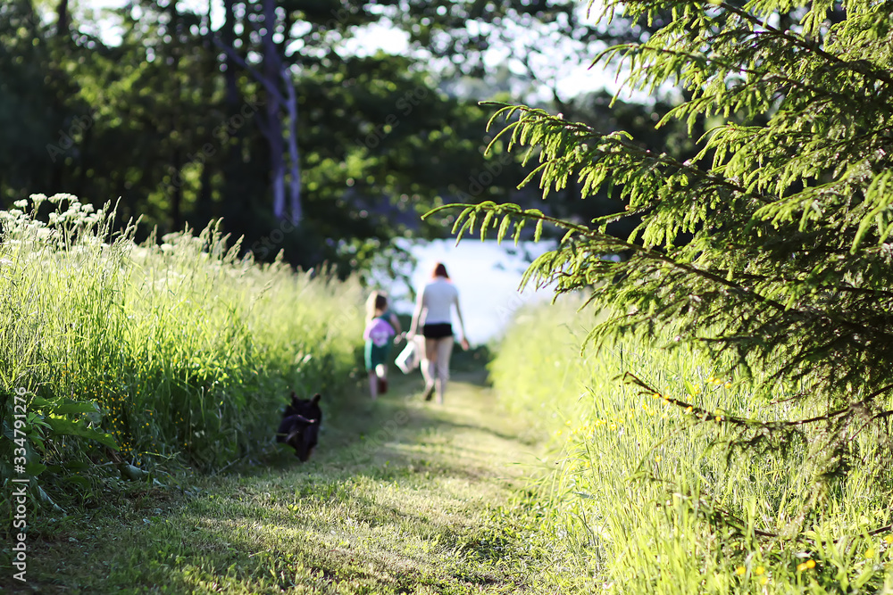 Two girls in summer dresses walking with small black dog on footpath in the green summer field Two girls in summer dresses walking with small black dog on footpath in the green summer field