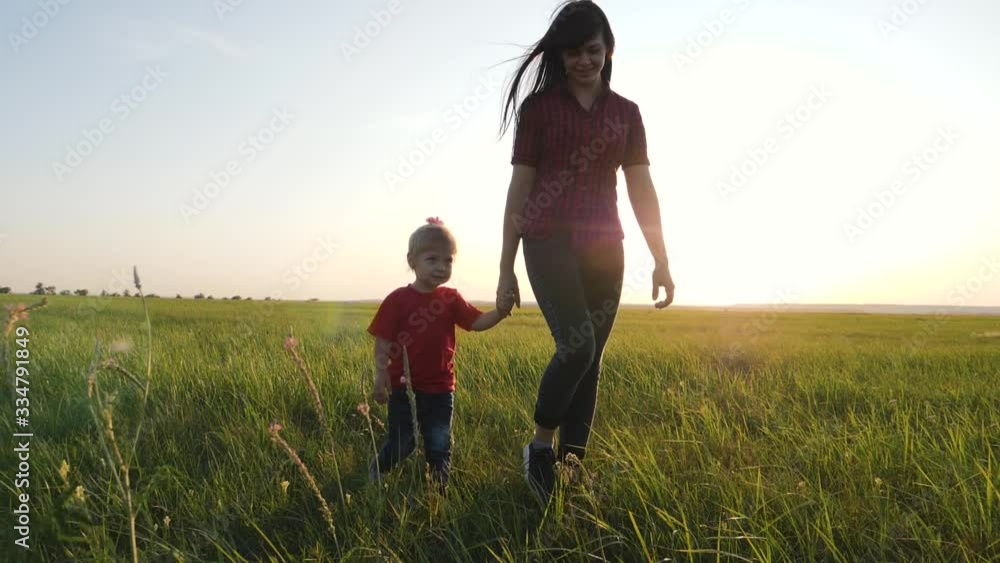 A young mother walks with her blonde daughter in the fresh air. Happy family walking on green grass. A young mother walks with her blonde daughter in the fresh air. Happy family walking on green grass.