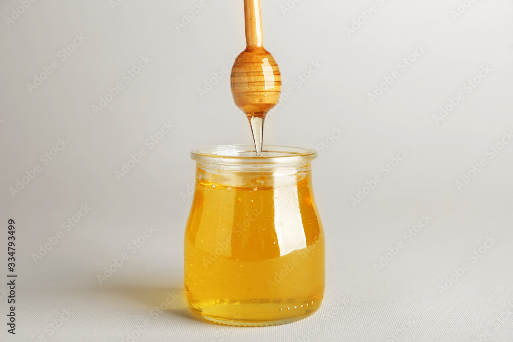 Sweet honey dripping from dipper in jar on light background Sweet honey dripping from dipper in jar on light background