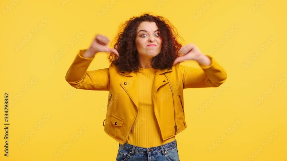 displeased girl showing thumbs down and grimacing isolated on yellow displeased girl showing thumbs down and grimacing isolated on yellow